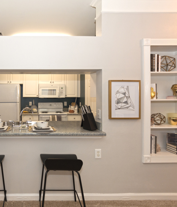 Apartment living space with breakfast bar and stools, built in bookshelves, and window to kitchen.