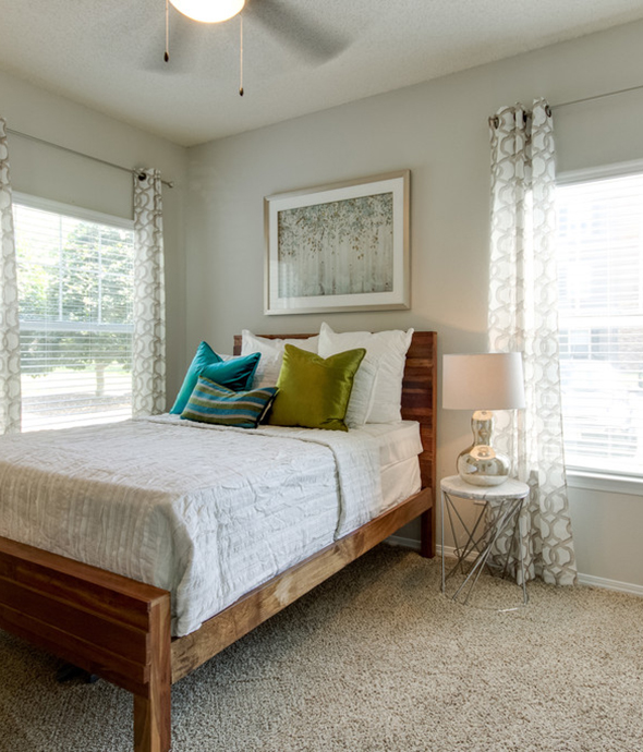 Bedroom with plush carpet, wood bed frame with comfortable bedding, large artwork, and corner windows.