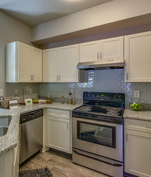 Kitchen with wood floor, white cabinets, gray counters, and stainless steel appliances.