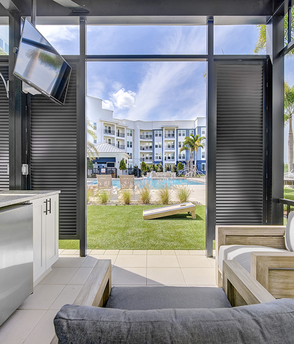 Outdoor lounge with plush seating, outdoor kitchen, TV, and bocce ball lawn with cornhole game.